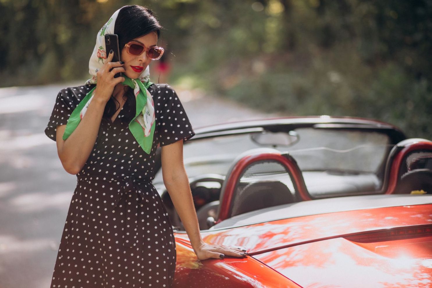 A woman standing beside a car dressed as someone from the 50s.